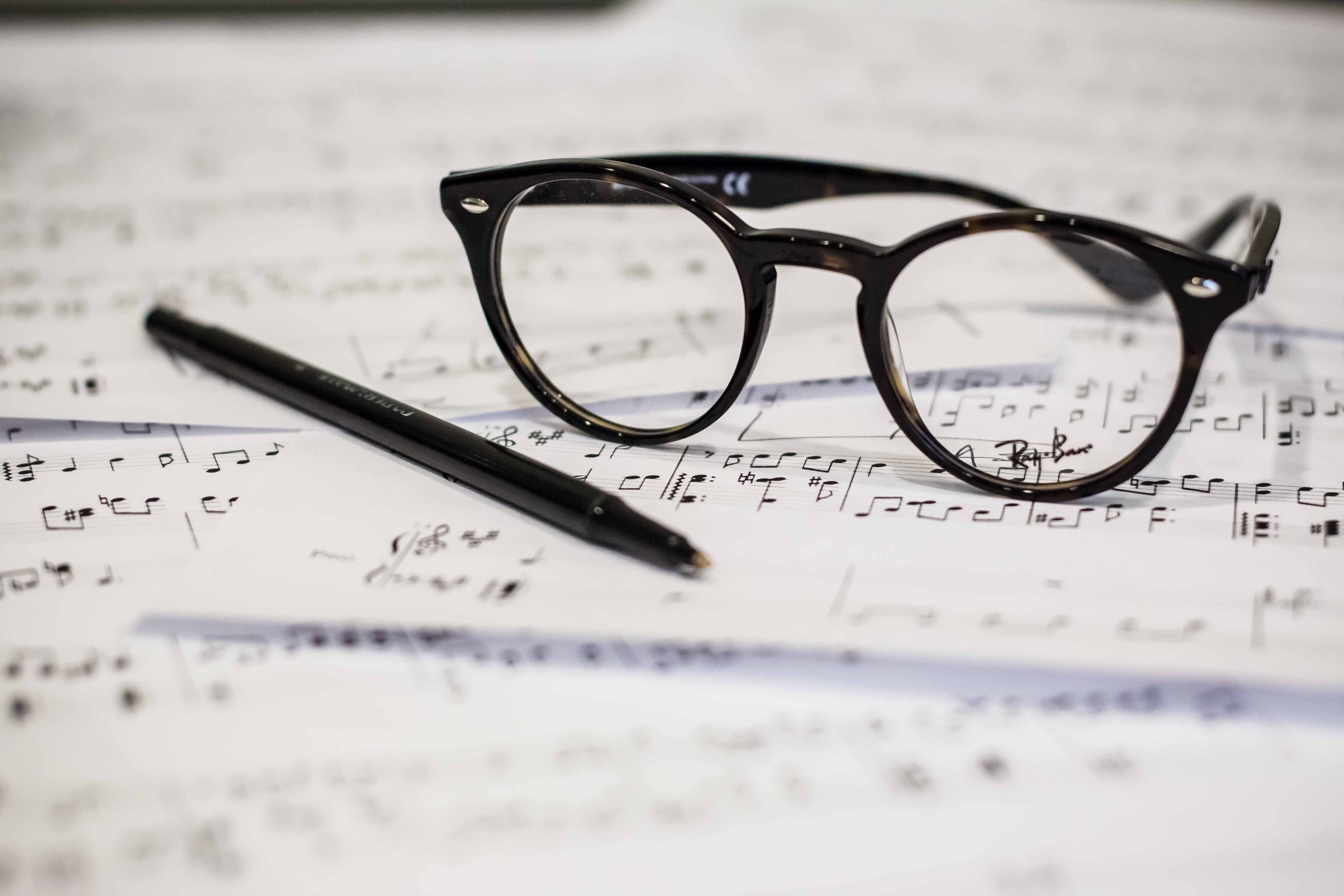 a picture of a pair of glasses and pen on top of a stack of handwritten sheet music